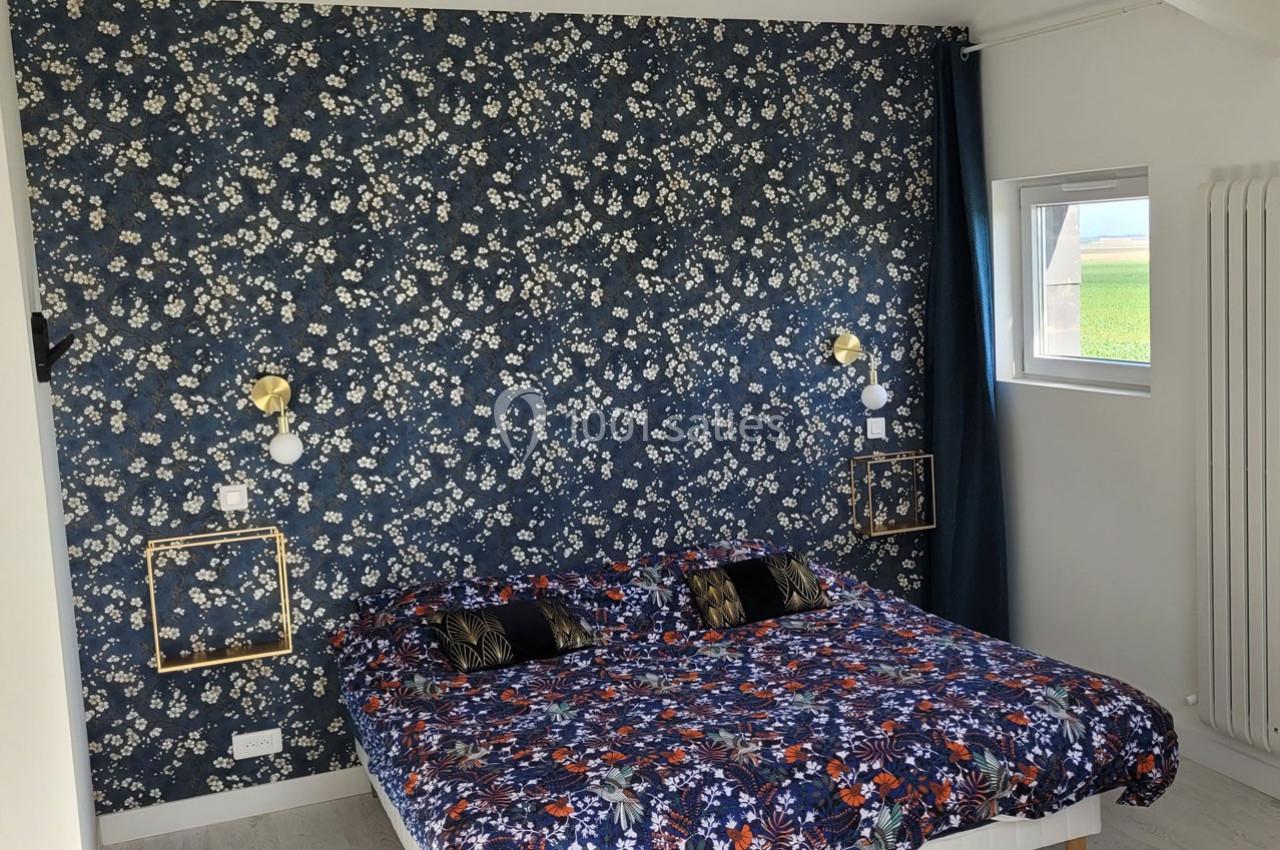 Location salle Bailleau-l'Évêque (Eure-et-Loir) - Le Domaine du Moulin 28 & SPA #32 Chambre avec un lit double, mur tapissé de motifs floraux bleus, luminaires dorés et fenêtre laissant entrer la lumière.