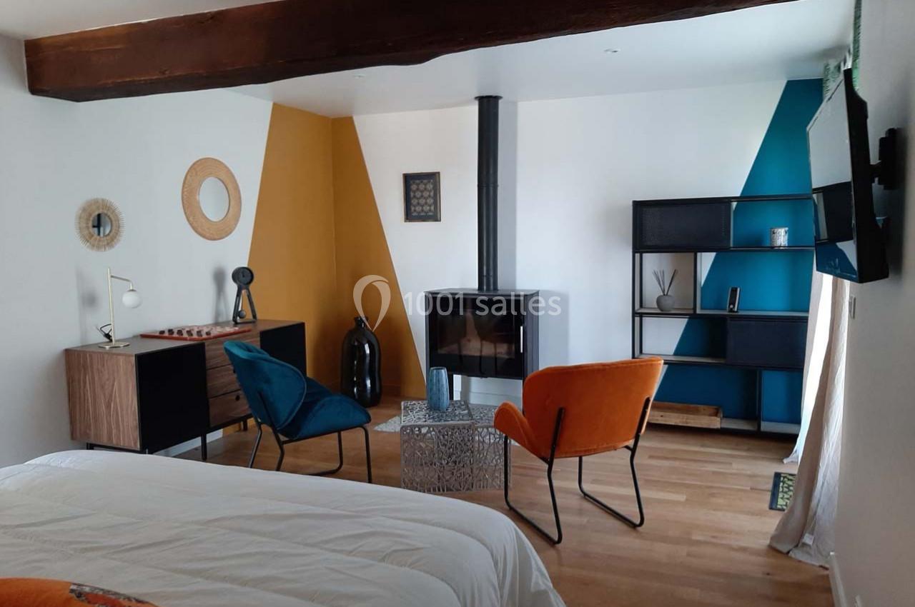 Location salle Bailleau-l'Évêque (Eure-et-Loir) - Le Domaine du Moulin 28 & SPA #26 Chambre moderne avec lit, poêle à bois, fauteuils colorés, étagère et murs aux motifs géométriques.