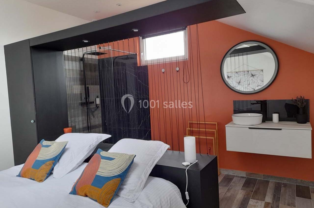 Location salle Bailleau-l'Évêque (Eure-et-Loir) - Le Domaine du Moulin 28 & SPA #31 Chambre moderne avec lit double, cloison ajourée, mur orange, salle de bain attenante et lavabo sur meuble suspendu.