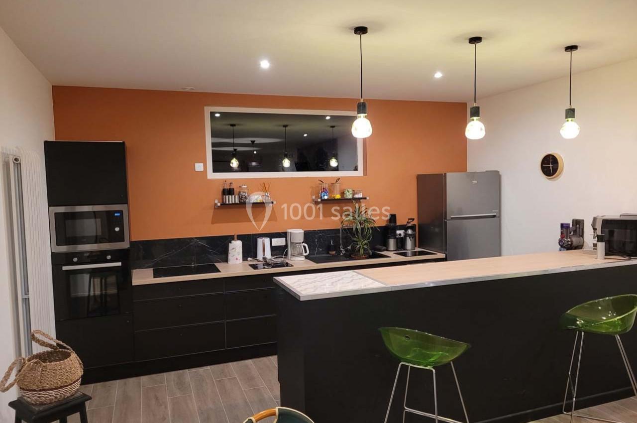 Location salle Bailleau-l'Évêque (Eure-et-Loir) - Le Domaine du Moulin 28 & SPA #21 Cuisine moderne avec mur orange, meubles noirs, plan de travail clair, électroménagers en inox et éclairage suspendu.