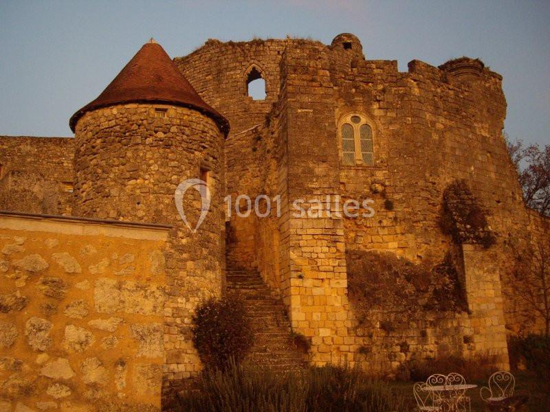 Vieille forteresse en pierre avec une tour ronde et des fenêtres, éclairée par une lumière chaude au coucher du soleil.