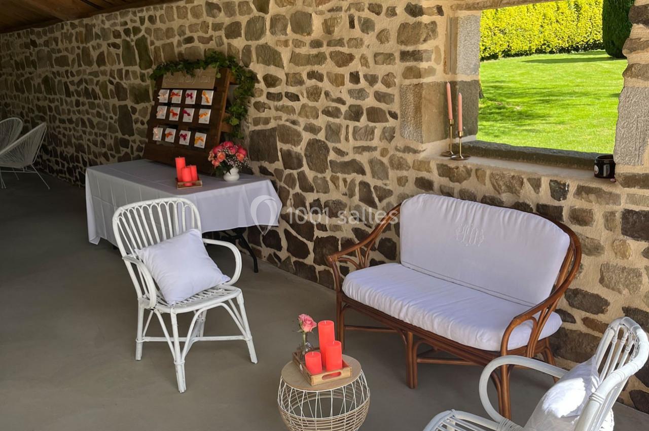 Espace extérieur aménagé avec des meubles en rotin, une table décorée et un présentoir sur un mur en pierre.