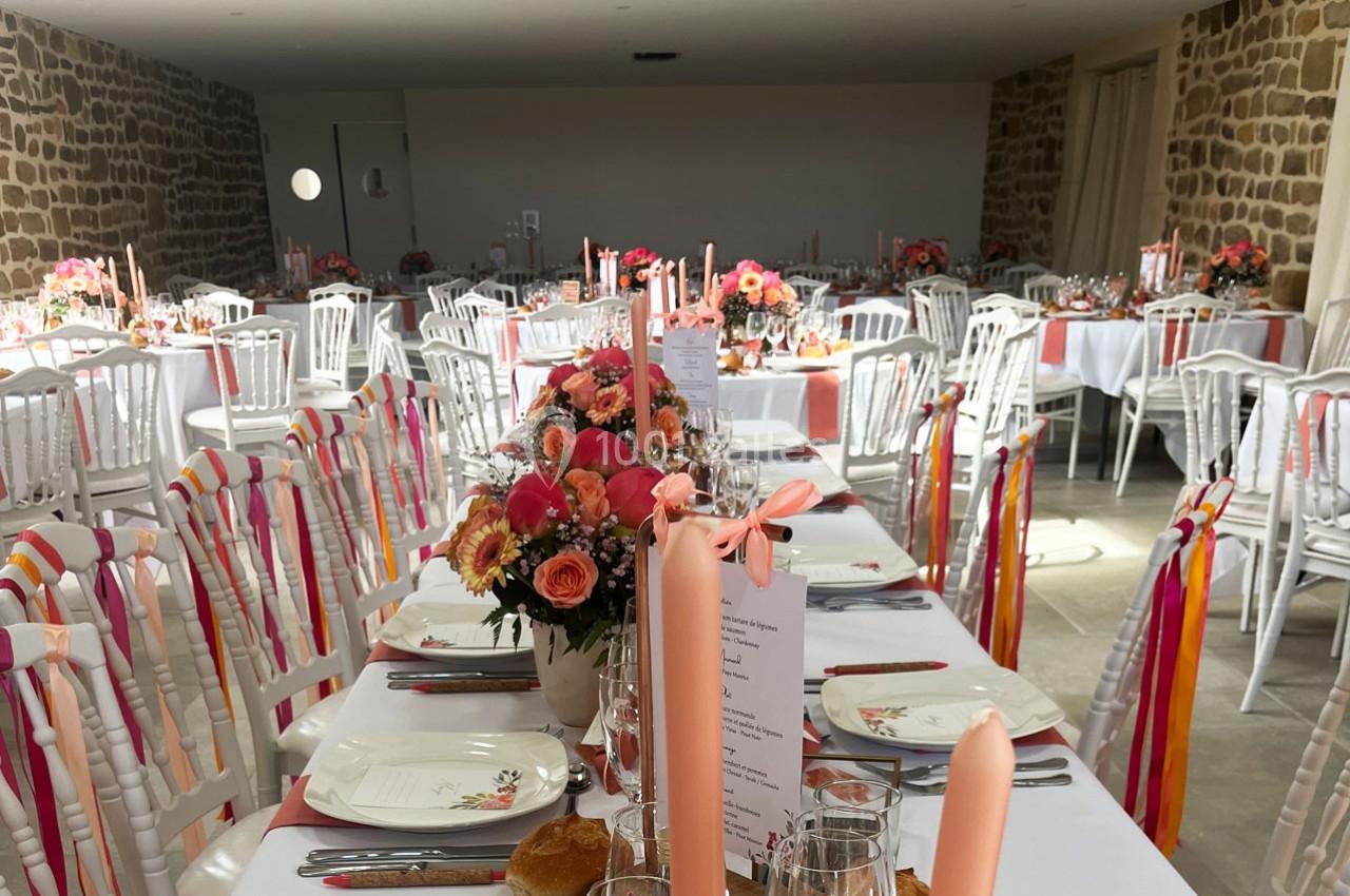 Salle de réception décorée avec des tables dressées, des fleurs colorées et des chaises ornées de rubans.