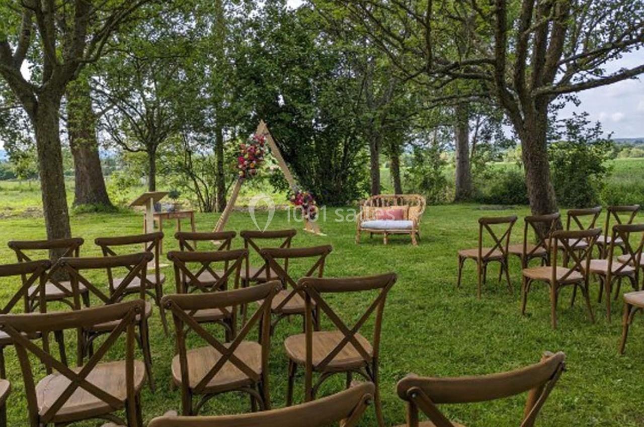 Chaises en bois disposées en extérieur face à une arche décorée de fleurs, entourées d'arbres et de verdure.