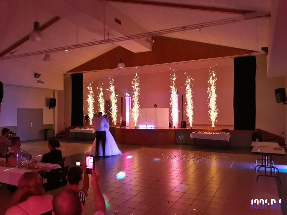 Un couple danse au centre d'une salle de réception illuminée par des jets d'étincelles sur la scène.