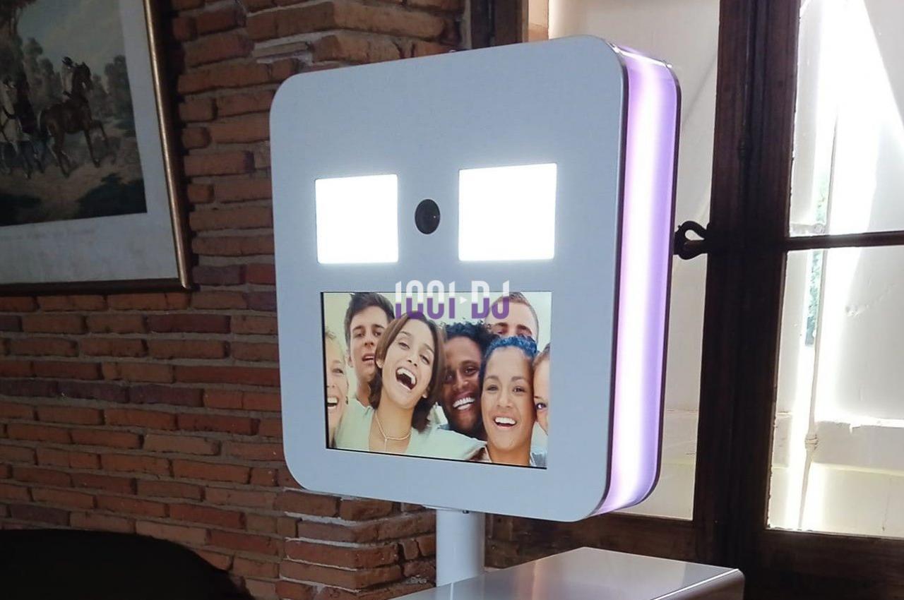 Borne photo avec écran affichant un groupe de personnes souriantes, installée dans une pièce lumineuse avec murs en briques.