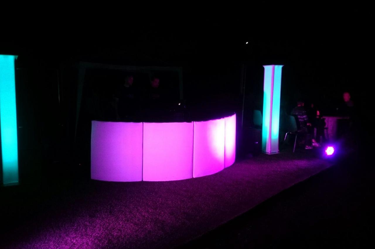 Installation lumineuse avec des colonnes et un comptoir éclairés en rose et bleu dans un environnement sombre.