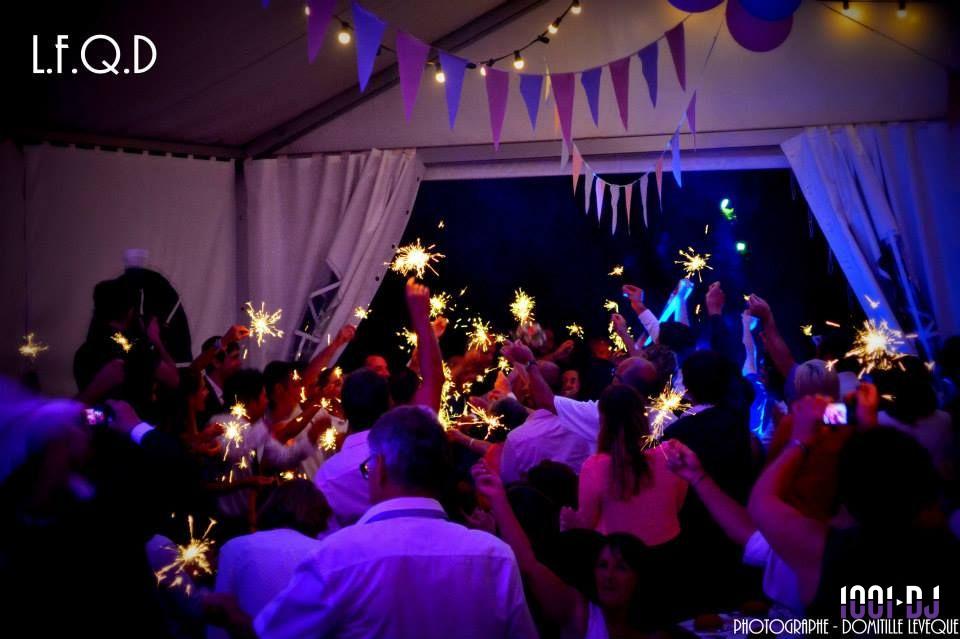 Des personnes dansent sous une tente décorée, tenant des cierges magiques allumés dans une ambiance festive.