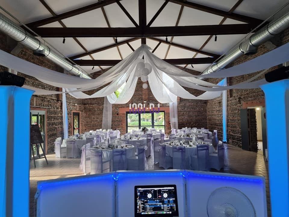 Salle de réception décorée avec des tables rondes, nappes blanches et voilages suspendus au plafond.