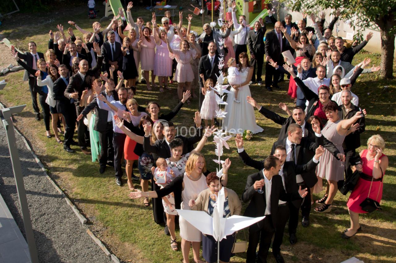 Groupe de personnes en tenue de cérémonie réunies à l'extérieur, souriant et levant les bras pour une photo festive.