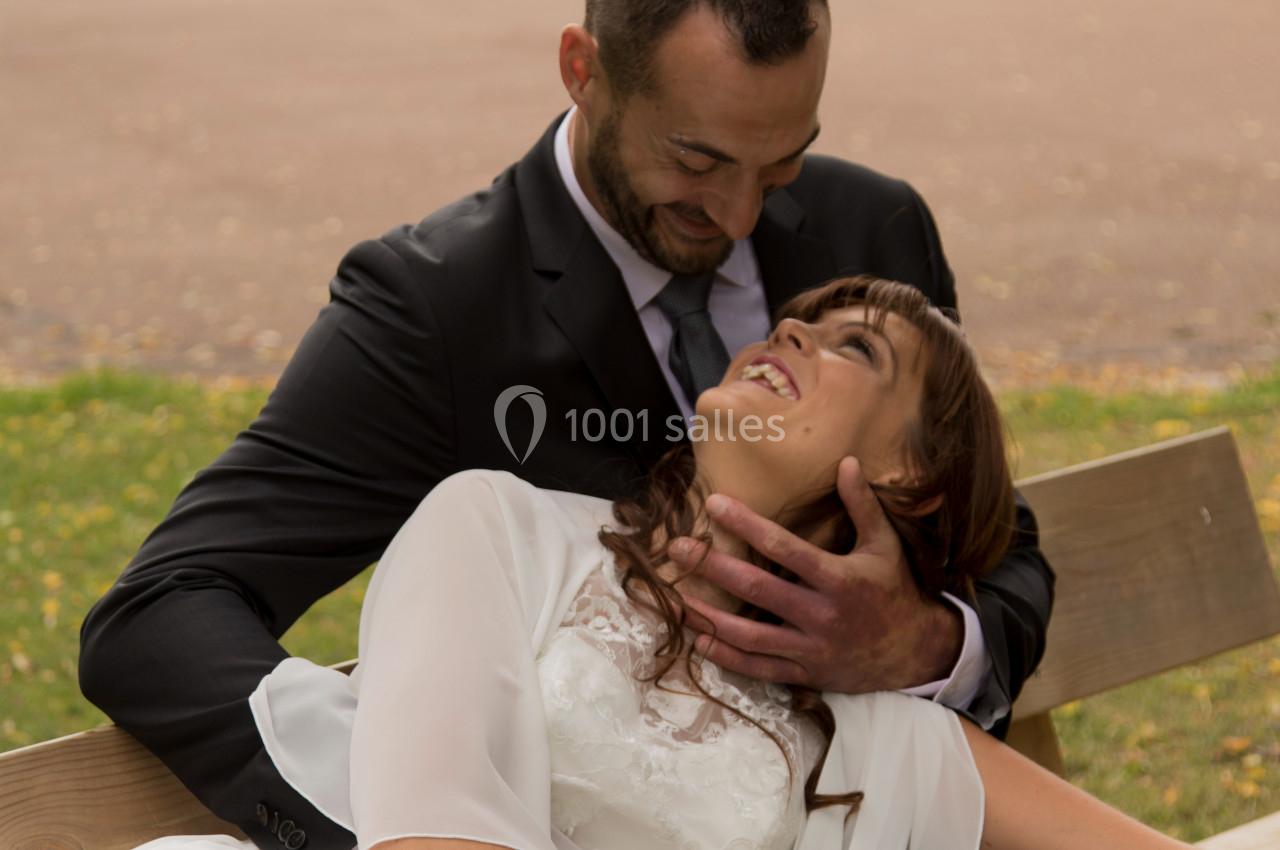 Un couple assis sur un banc, l'homme en costume sourit en regardant la femme en robe blanche allongée sur ses genoux.