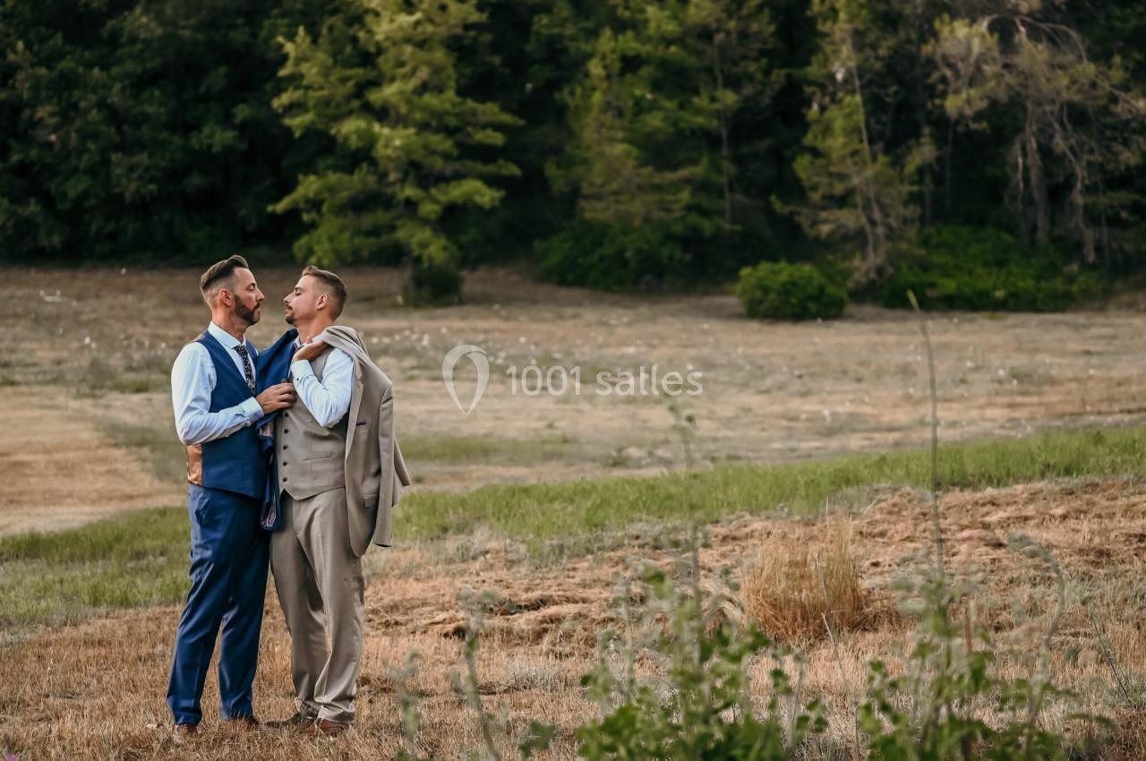 Deux hommes en costume se tiennent debout dans un champ, souriant l'un à l'autre, avec des arbres en arrière-plan.