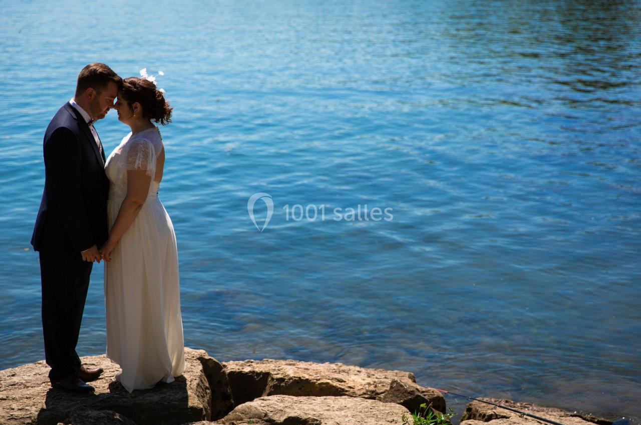 Un couple en tenue de mariage se tient la main sur des rochers au bord d'un lac sous un ciel dégagé.