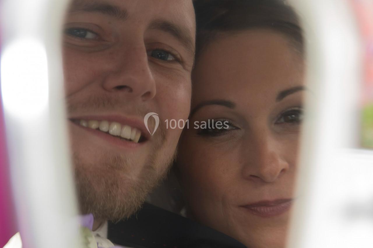 Un couple souriant photographié de près, partiellement encadré par un élément flou au premier plan.