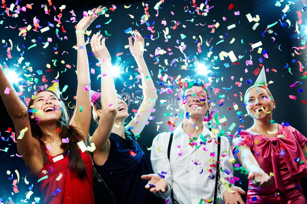 Quatre personnes souriantes célèbrent sous une pluie de confettis colorés, éclairées par des projecteurs.