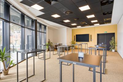 Façade moderne d'un hôtel Mercure avec des voitures circulant devant, entouré d'arbres et d'un ciel partiellement nuageux.