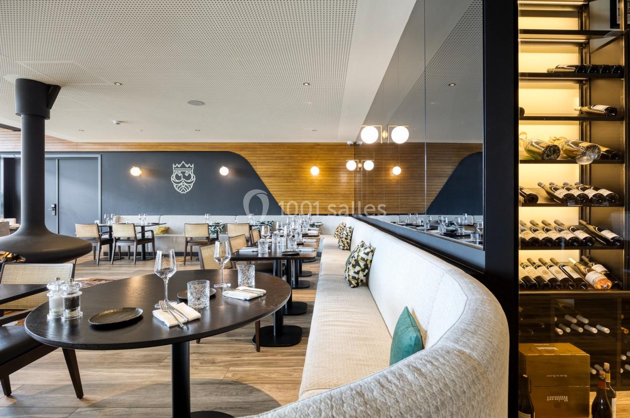 Salle de restaurant moderne avec tables dressées, banquettes, éclairage suspendu et étagères à vin.