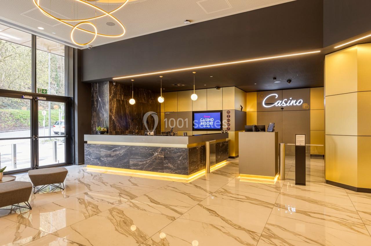 Accueil d'un casino moderne avec comptoir en marbre, éclairage design et grandes baies vitrées donnant sur l'extérieur.