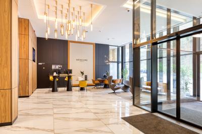 Façade moderne d'un hôtel Mercure avec des voitures circulant devant, entouré d'arbres et d'un ciel partiellement nuageux.