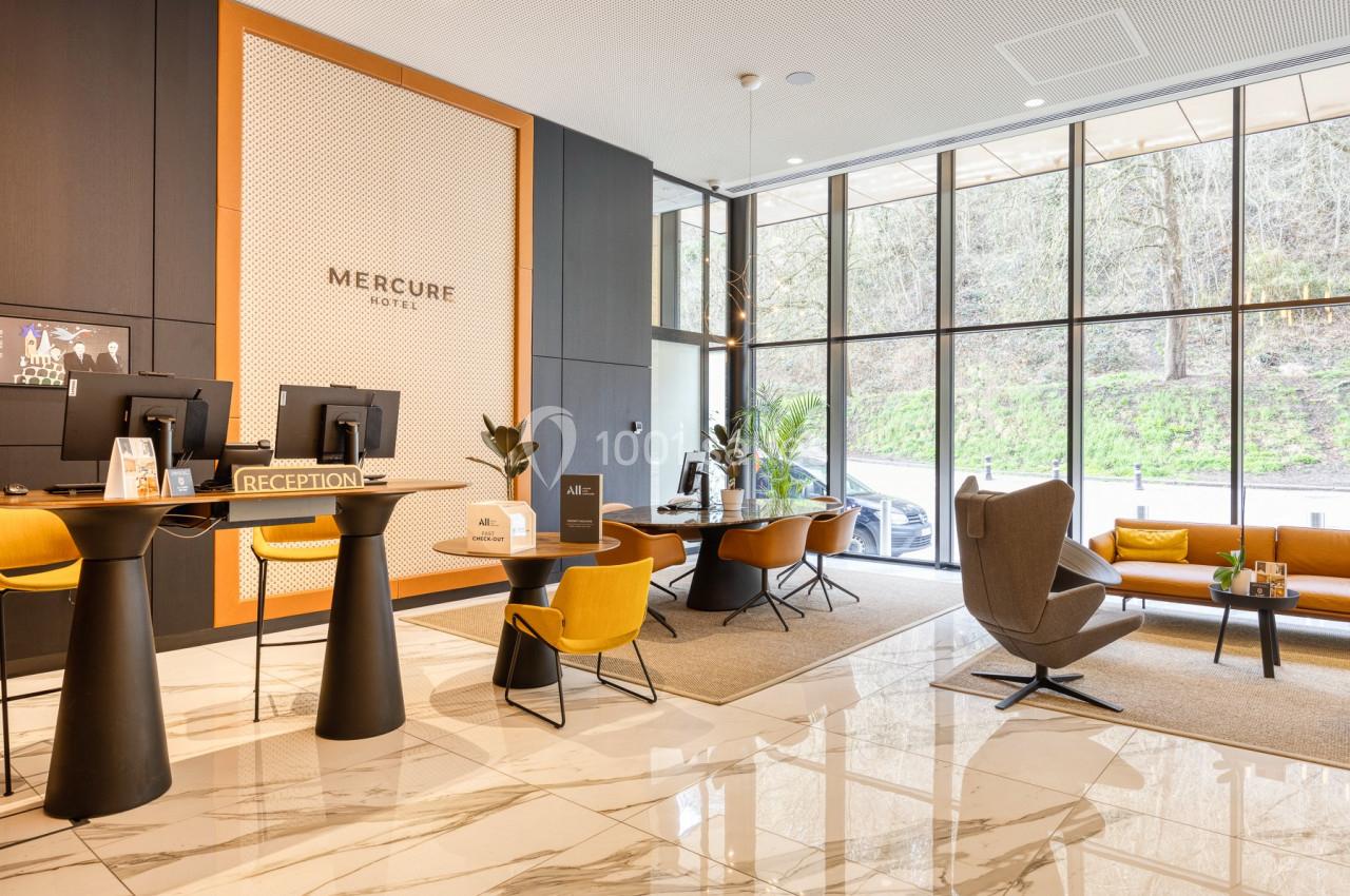 Hall d'accueil moderne avec comptoirs de réception, fauteuils design, grandes baies vitrées et sol en marbre.