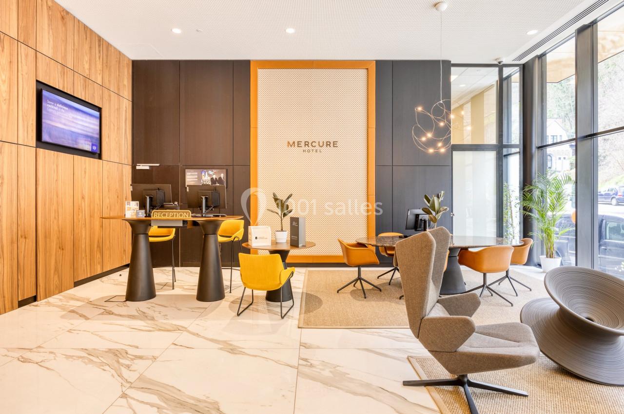 Hall d'accueil moderne avec comptoir de réception, fauteuils design, éclairage suspendu et grandes baies vitrées.