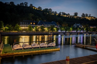 Miniature Location salle Namur (Province de Namur) - Casino Resort Namur #28 Vue sur une rivière bordée de bateaux, avec des bâtiments historiques et une colline boisée en arrière-plan.