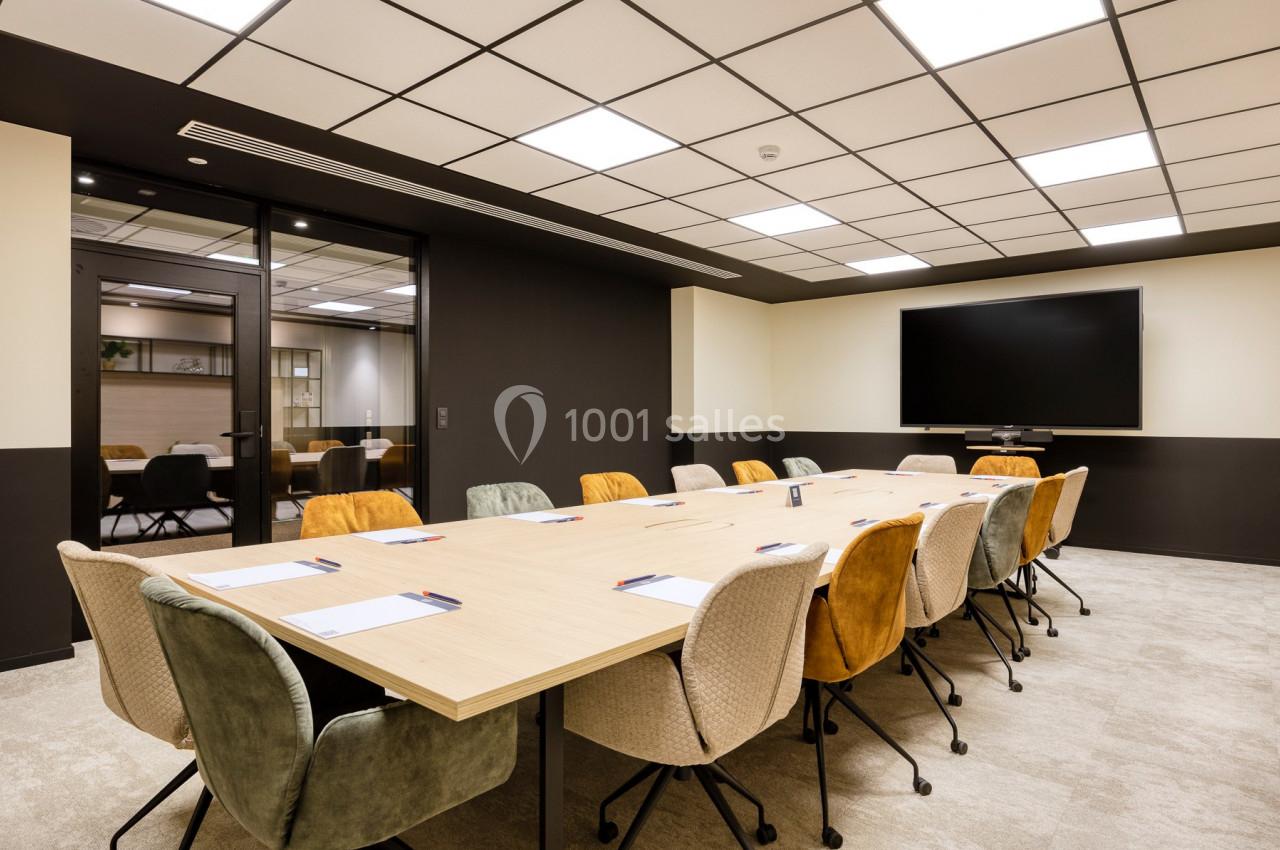 Location salle Namur (Namur) - Casino Resort Namur #2 Salle de réunion moderne avec une grande table rectangulaire entourée de chaises colorées et un écran mural.