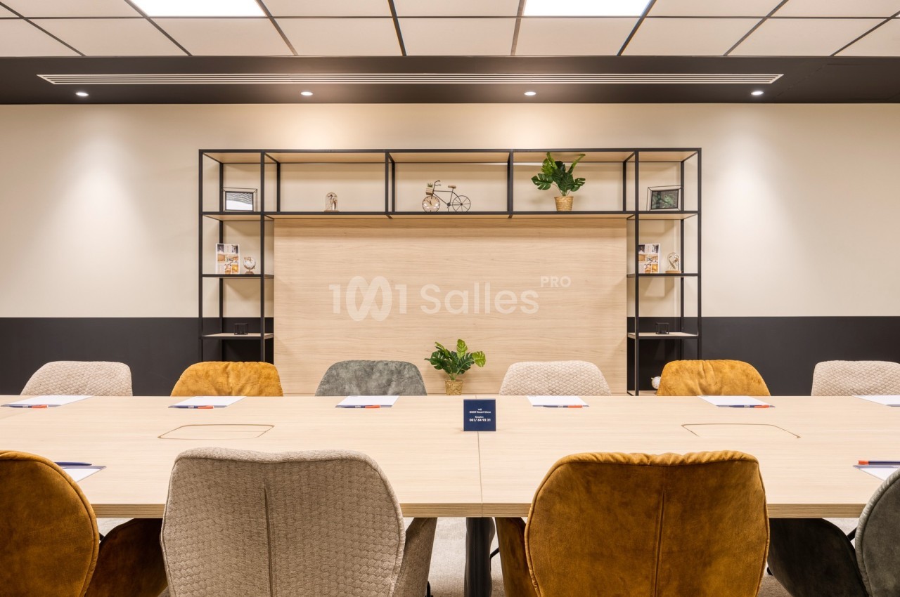 Salle de réunion avec une grande table en bois, des chaises colorées et une étagère décorative en arrière-plan.