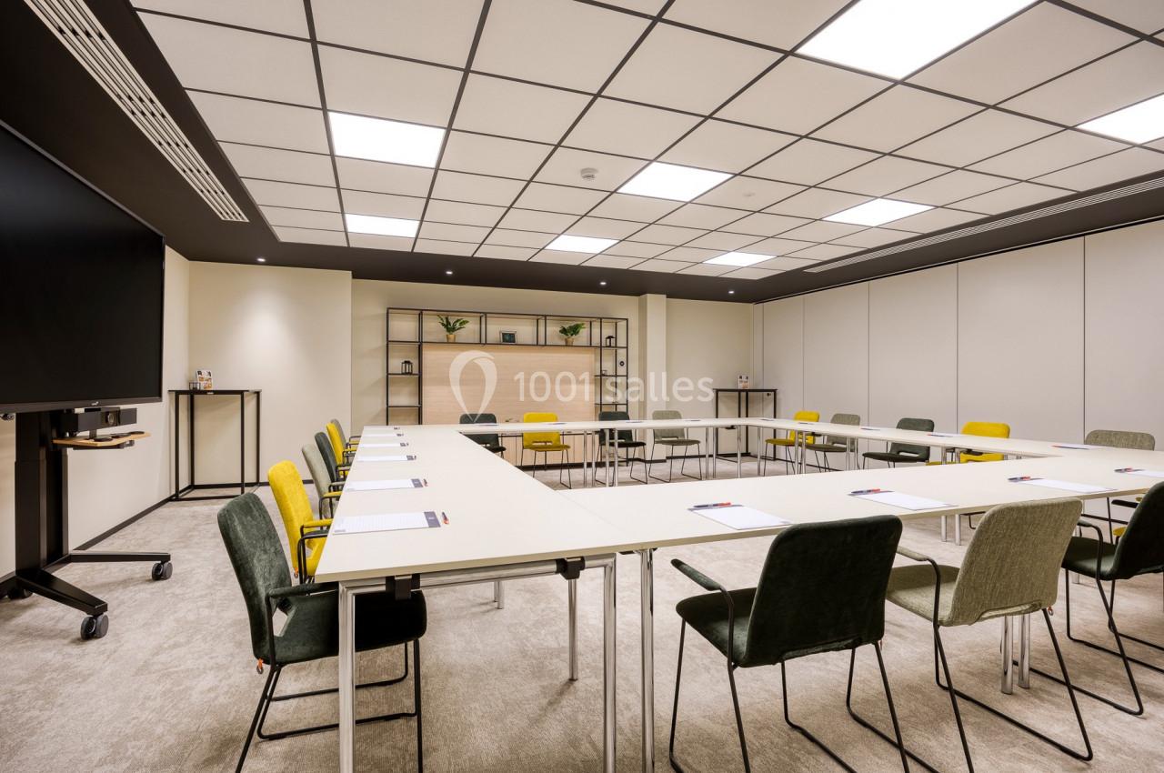 Location salle Namur (Namur) - Casino Resort Namur #5 Salle de réunion lumineuse avec tables disposées en U, chaises colorées et étagères décoratives en arrière-plan.