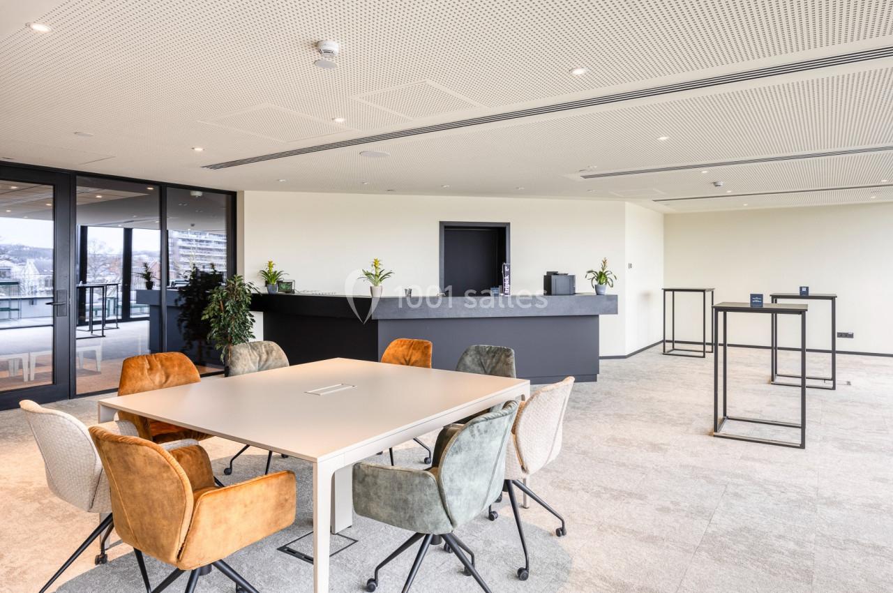 Location salle Namur (Namur) - Casino Resort Namur #11 Salle de réunion lumineuse avec table centrale, chaises colorées et comptoir en arrière-plan.