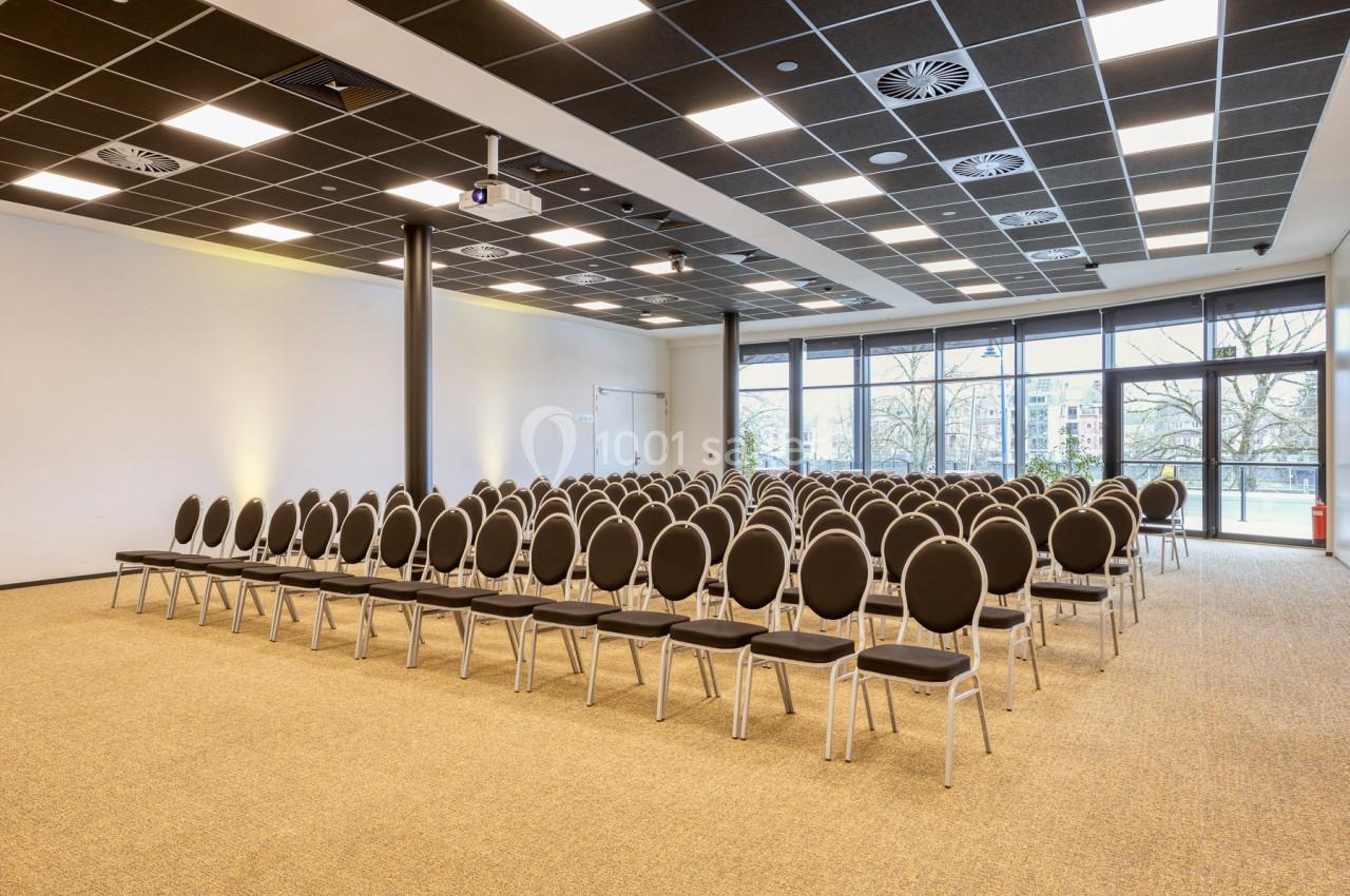 Location salle Namur (Namur) - Casino Resort Namur #12 Salle de conférence lumineuse avec des rangées de chaises noires alignées face à un écran de projection.