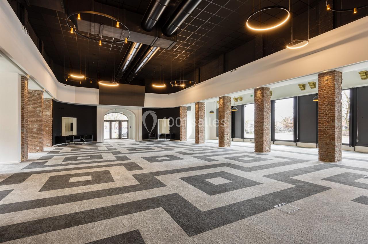 Location salle Namur (Namur) - Casino Resort Namur #17 Salle spacieuse avec sol à motifs géométriques, colonnes en briques, grandes fenêtres et luminaires suspendus.