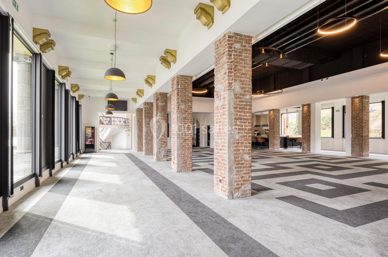 Location salle Namur (Namur) - Casino Resort Namur #19 Salle lumineuse avec colonnes en briques, grandes baies vitrées, sol en motifs géométriques et plafonniers suspendus.