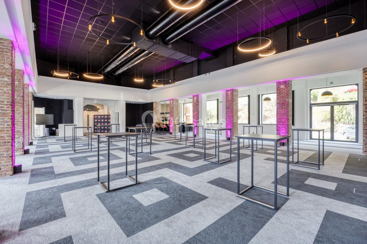 Location salle Namur (Namur) - Casino Resort Namur #27 Salle moderne avec un sol à motifs géométriques, des tables hautes métalliques et un éclairage suspendu circulaire.