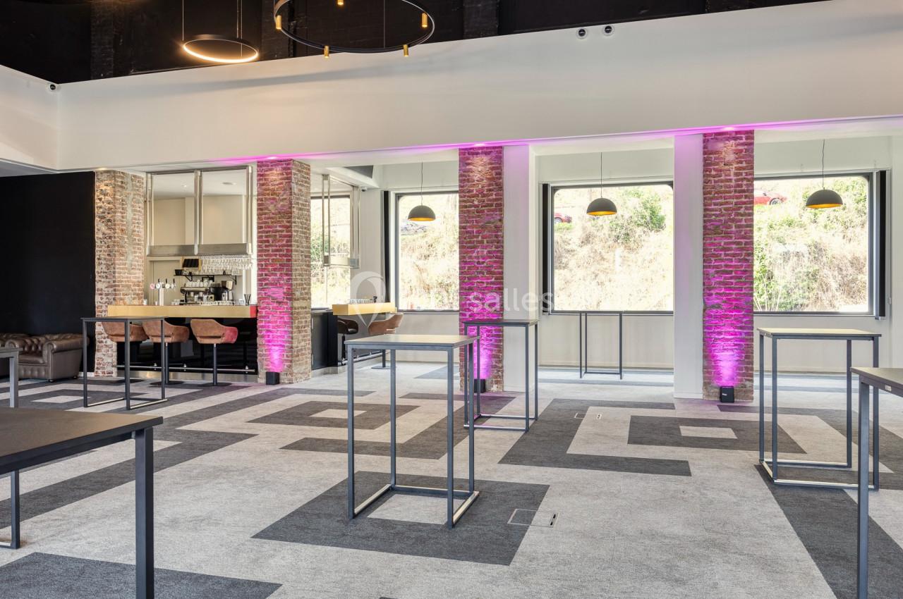 Location salle Namur (Namur) - Casino Resort Namur #29 Salle lumineuse avec murs en briques, bar équipé, tables hautes et éclairage violet décoratif.