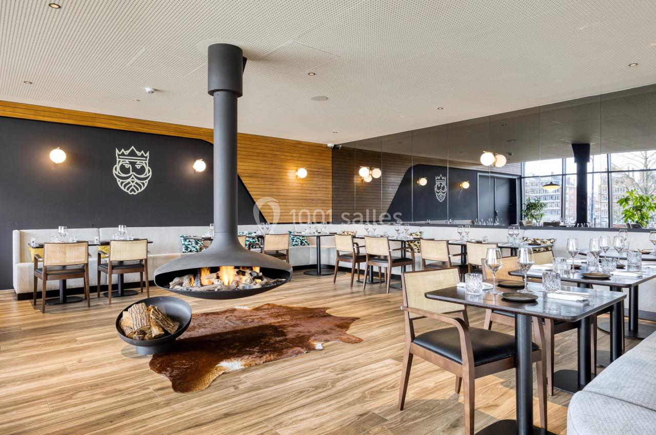 Location salle Namur (Namur) - Casino Resort Namur #30 Salle de restaurant moderne avec cheminée suspendue, tables dressées et décoration élégante sur fond de bois et miroirs.