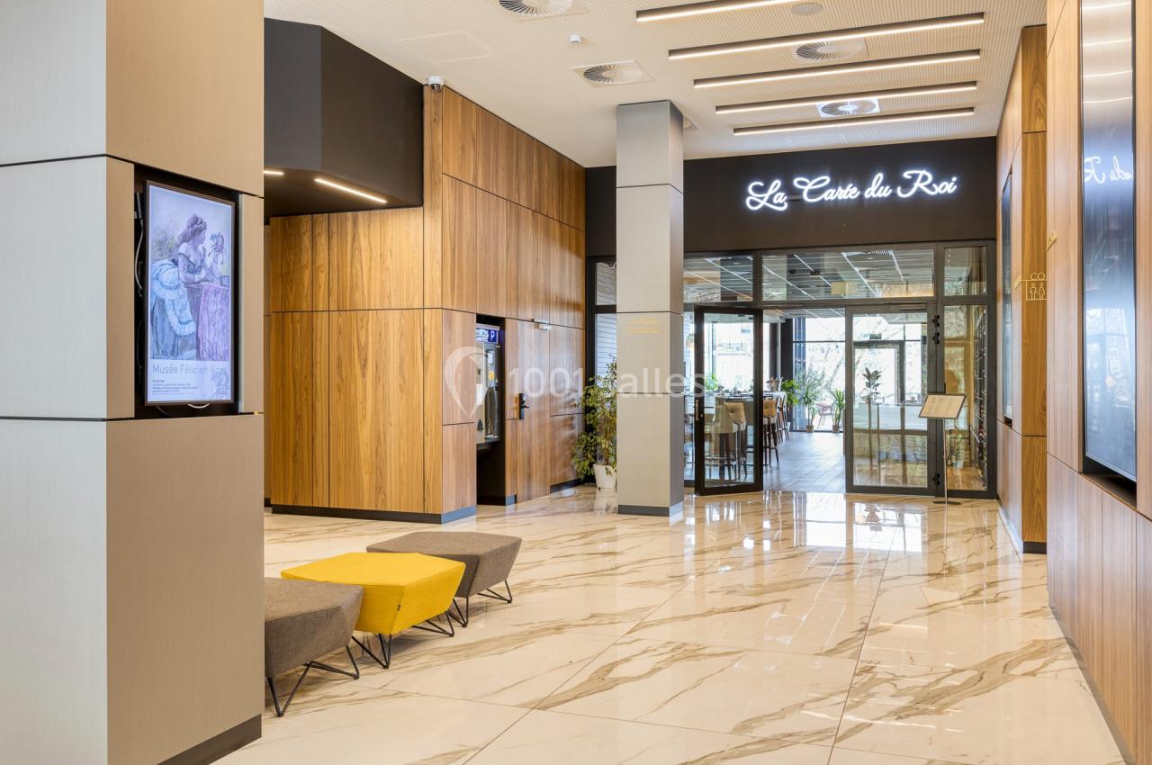 Location salle Namur (Namur) - Casino Resort Namur #44 Entrée d'un restaurant avec sol en marbre, murs en bois, bancs jaunes et gris, et enseigne lumineuse.