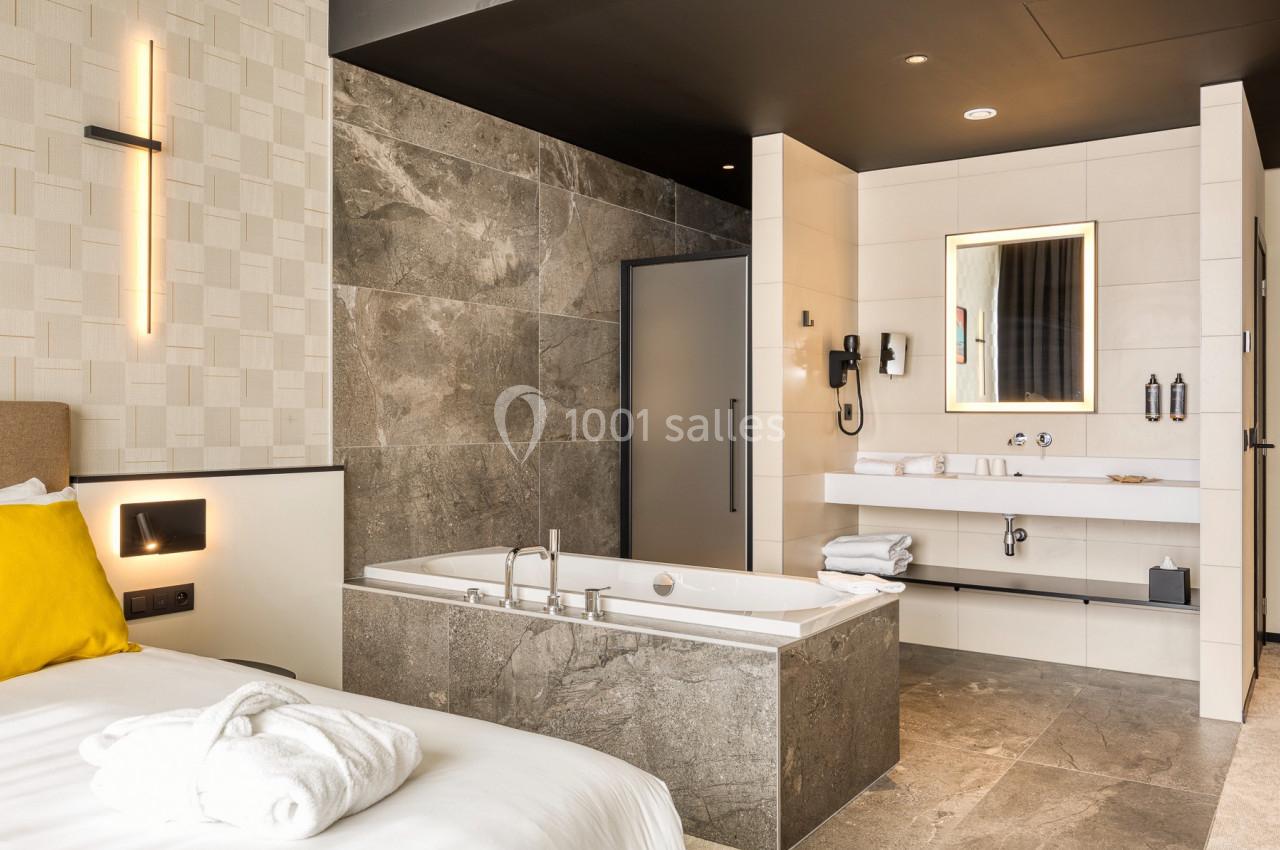 Location salle Namur (Namur) - Casino Resort Namur #45 Salle de bain moderne avec baignoire en pierre, lavabo, miroir éclairé et décorations murales élégantes.