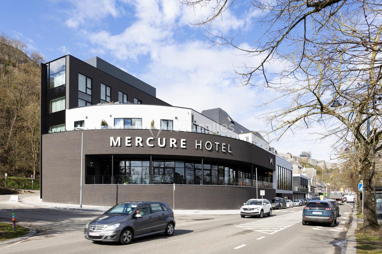 Location salle Namur (Namur) - Casino Resort Namur #49 Façade moderne d'un hôtel Mercure avec des voitures circulant sur une route adjacente, entouré d'arbres et de collines.