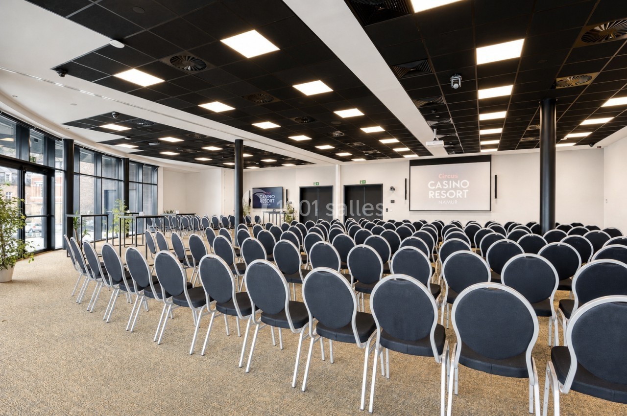Location salle Namur (Province de Namur) - Casino Resort Namur #17 Salle de conférence moderne avec rangées de chaises alignées, écran de projection et grandes baies vitrées.