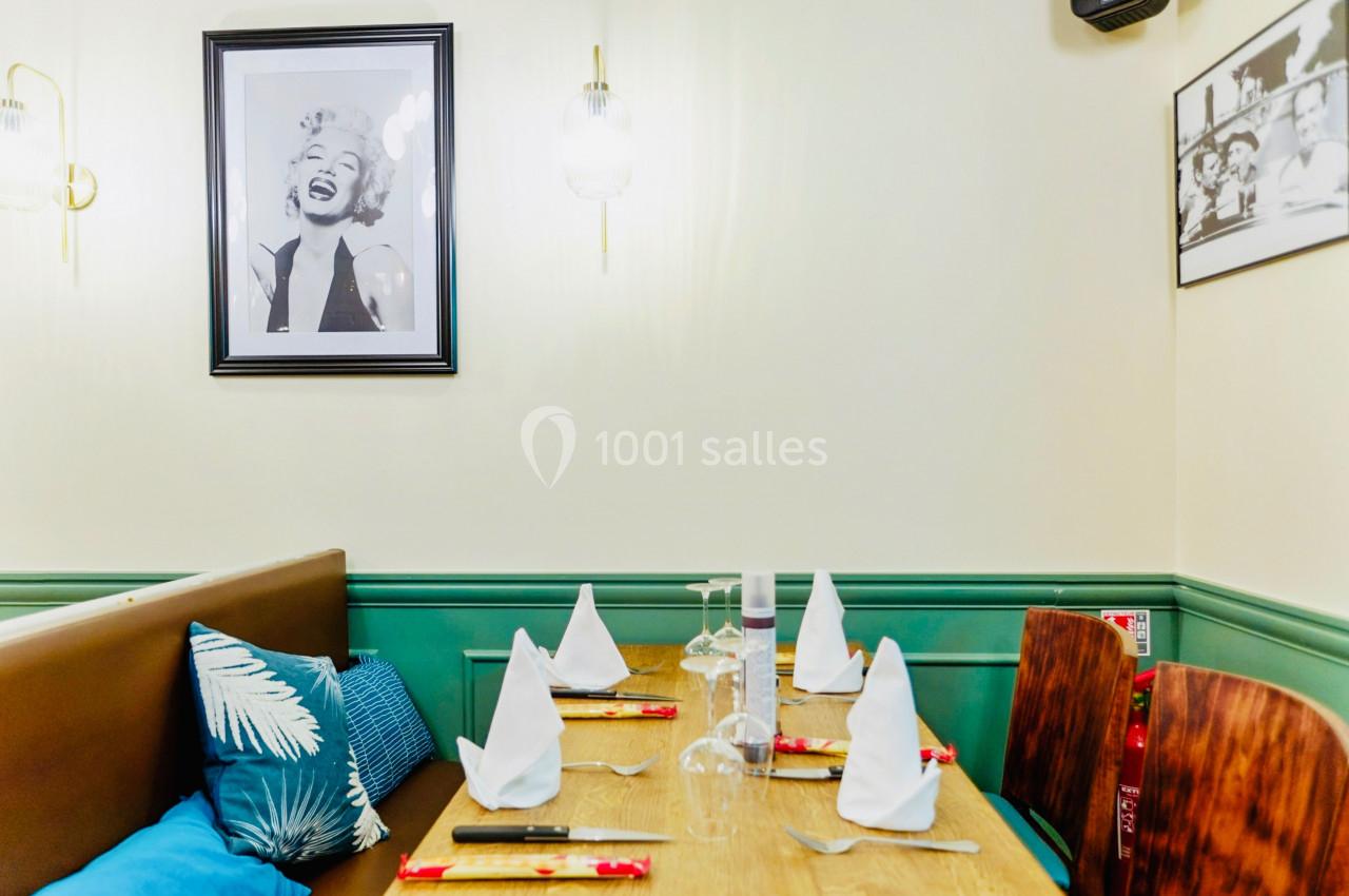 Table dressée avec serviettes pliées, verres et couverts dans un restaurant décoré de photos encadrées au mur.