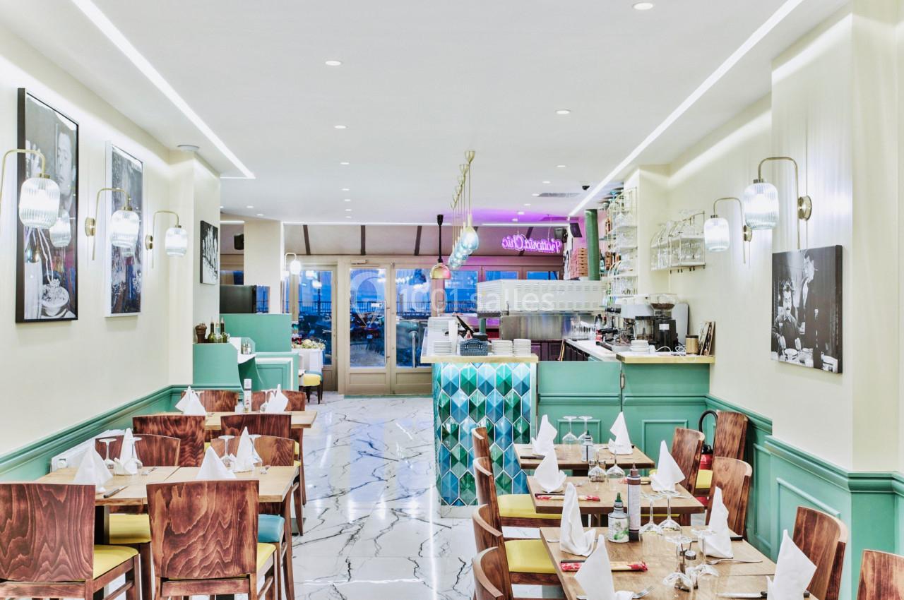 Salle de restaurant lumineuse avec tables dressées, décor moderne aux tons pastel et comptoir en arrière-plan.