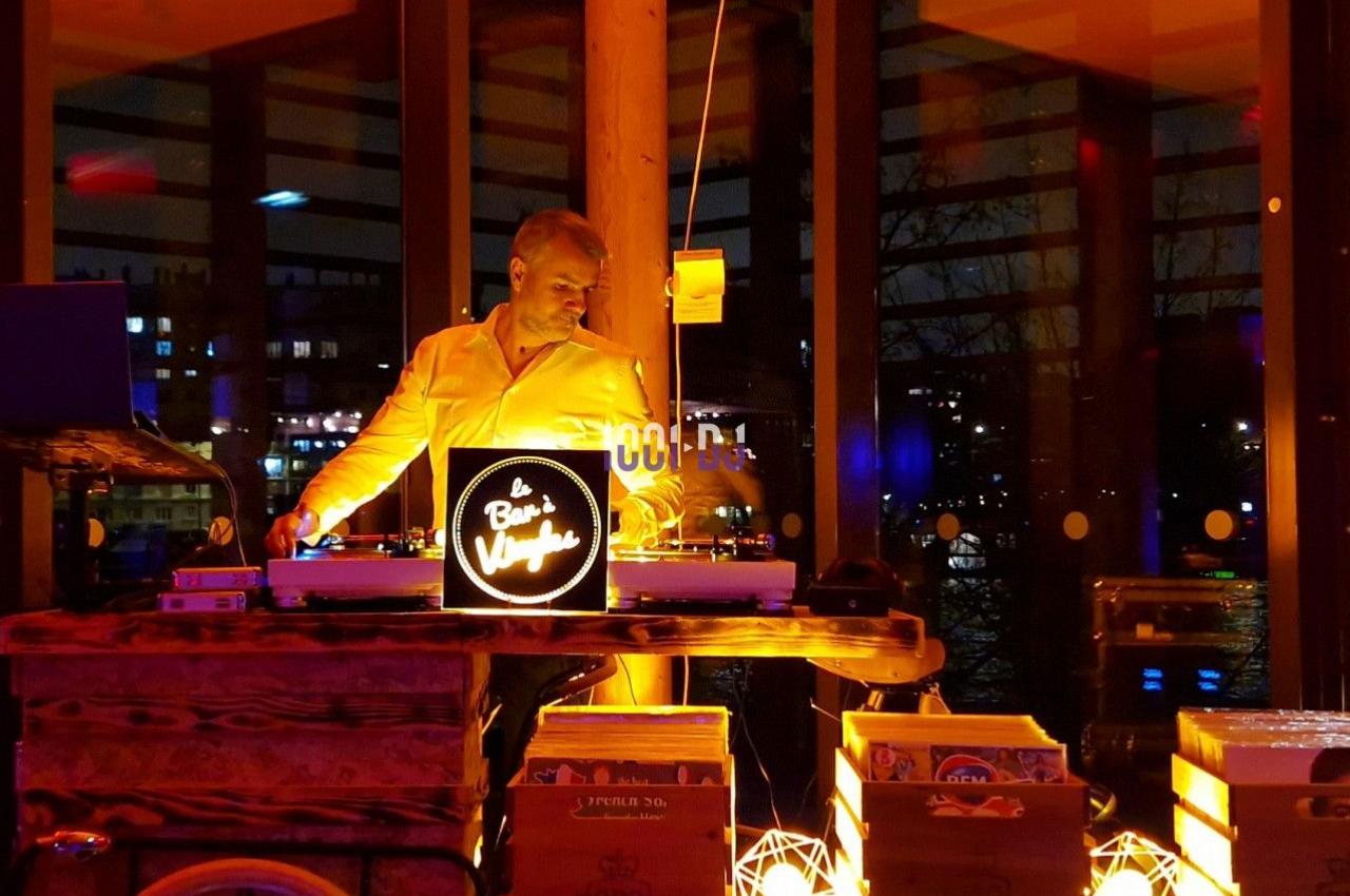 Un DJ mixe de la musique sur un vélo aménagé, entouré de lumières chaleureuses dans un espace vitré en soirée.