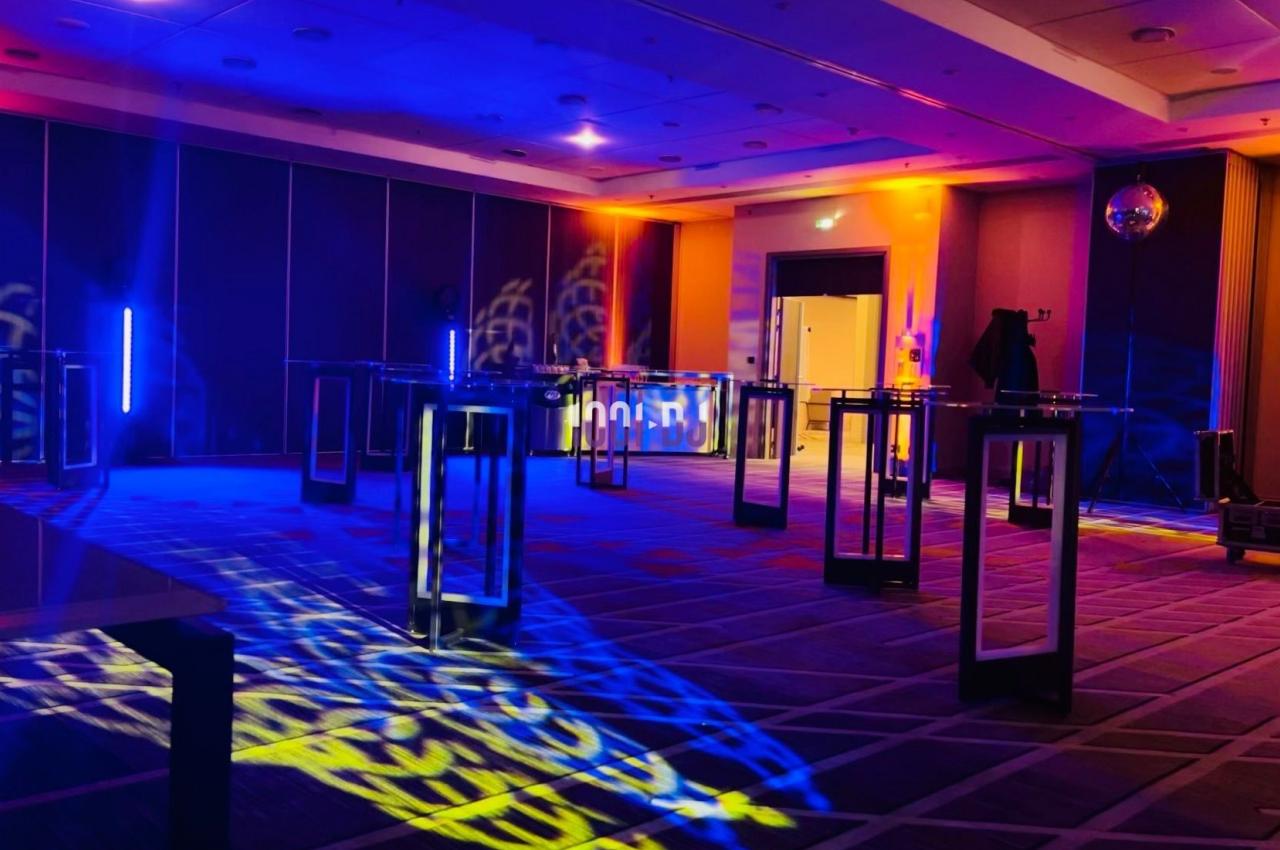 Salle de réception avec éclairage coloré, tables hautes et ambiance festive.