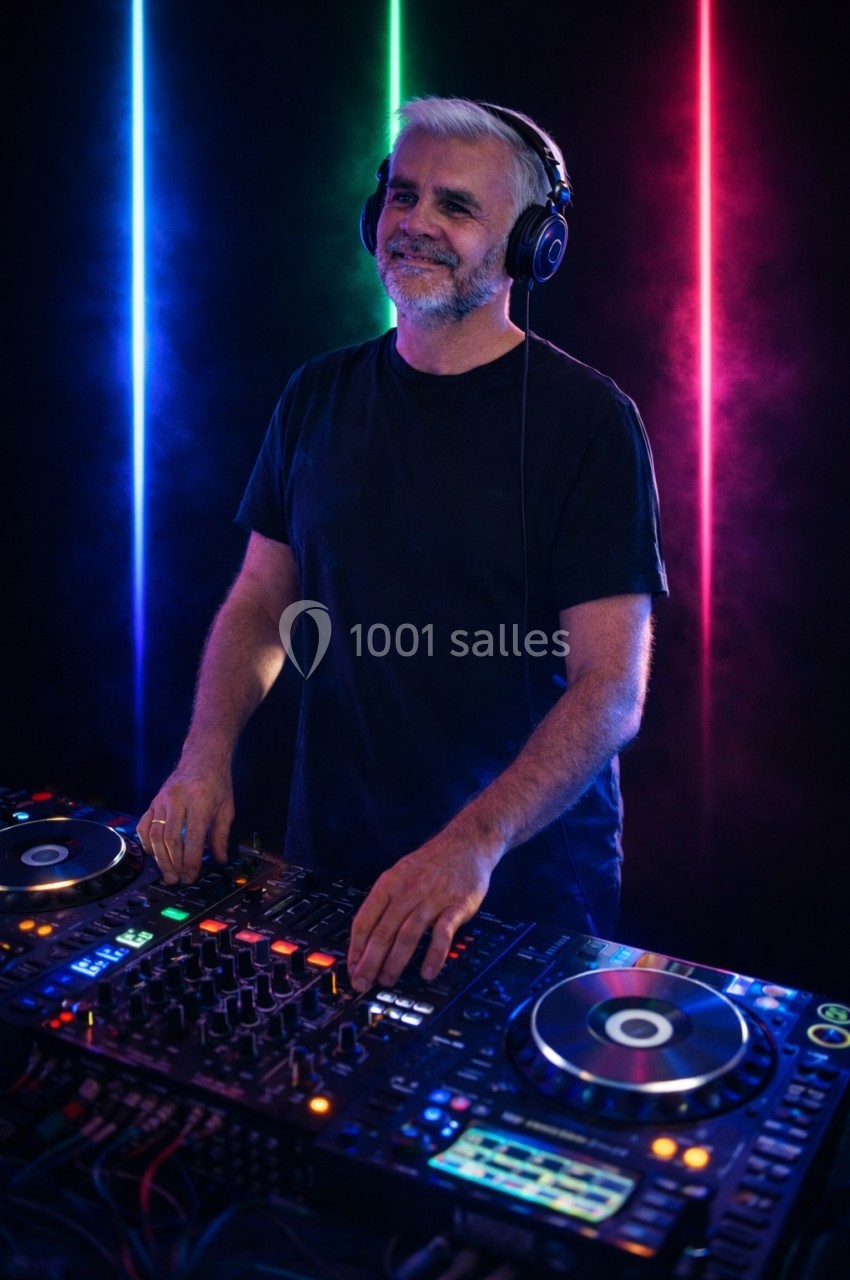 Un DJ souriant mixe de la musique sur une table de mixage, éclairé par des lumières colorées en arrière-plan.
