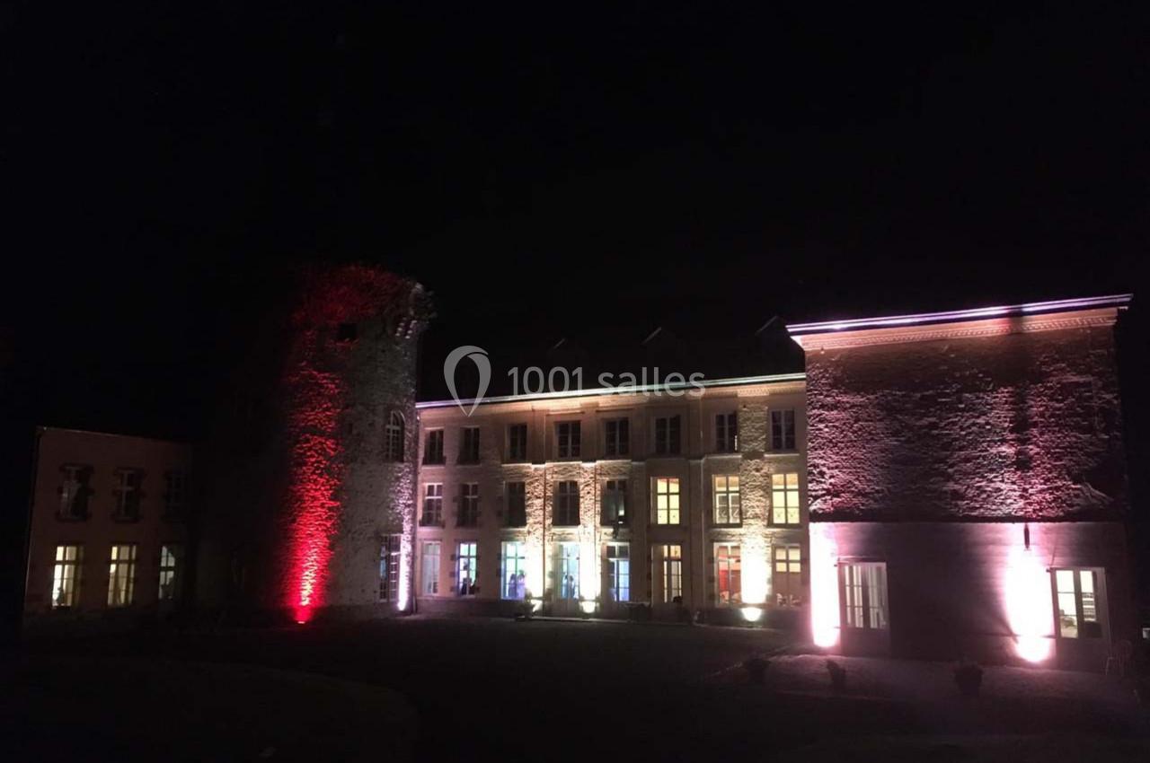 Façade d'un bâtiment historique éclairée de lumières colorées la nuit, avec une tour en pierre à gauche.