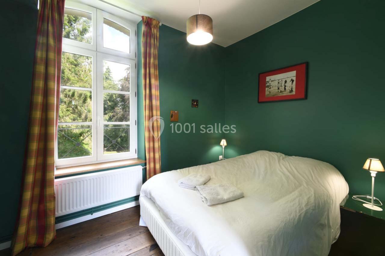 Chambre avec murs verts, lit double, fenêtre lumineuse avec rideaux à carreaux, et éclairage doux.