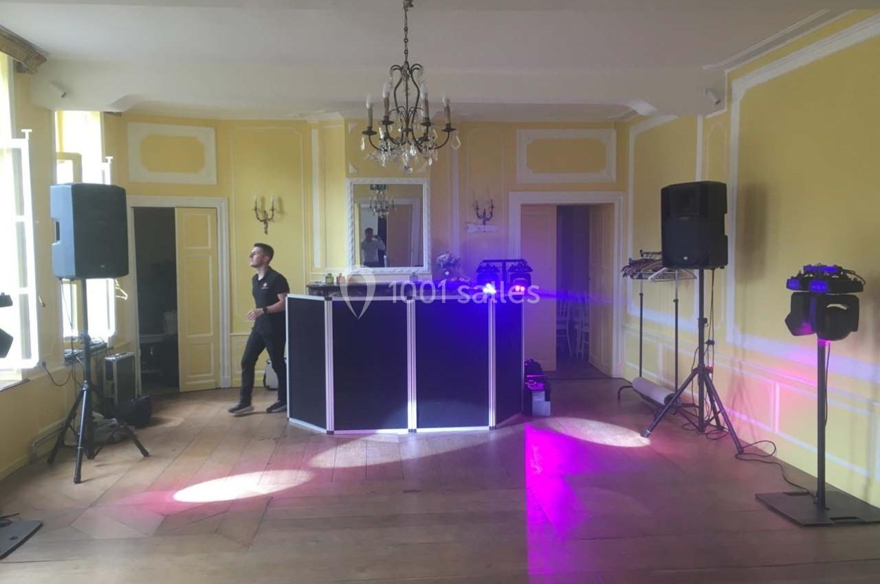 Salle lumineuse avec murs jaunes, parquet en bois, équipement de DJ installé et éclairage violet.