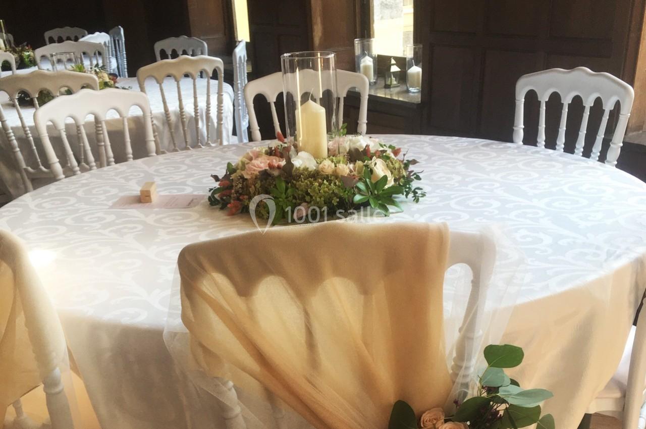 Table ronde décorée pour un événement, avec nappe blanche, centre de table floral et bougie cylindrique.