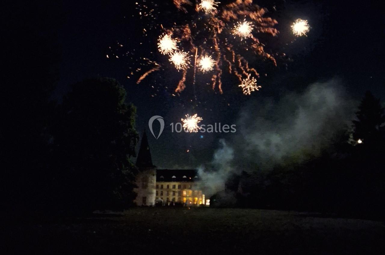 Feu d'artifice illuminant le ciel nocturne au-dessus d'un bâtiment éclairé entouré d'arbres.